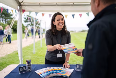 Admissions officer handing out prospectuses at an open-day stand — Person `main_image`, staff/administration.